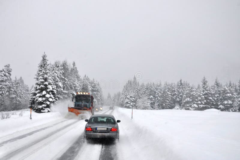 Tráfego difícil após nevar O líquido de limpeza da neve limpa operativamente a estrada coberto de neve da montanha imagem de stock royalty free Tráfego difícil após nevar O líquido de limpeza da neve limpa operativamente a estrada coberto de neve da montanha imagem de stock royalty free