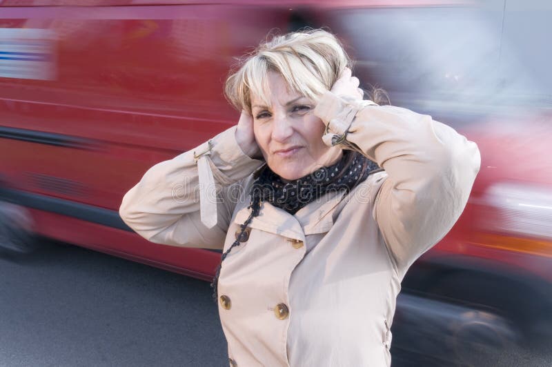 Mature woman with hands at the ears because of the loud noise of the street in the city. Mature woman with hands at the ears because of the loud noise of the street in the city.