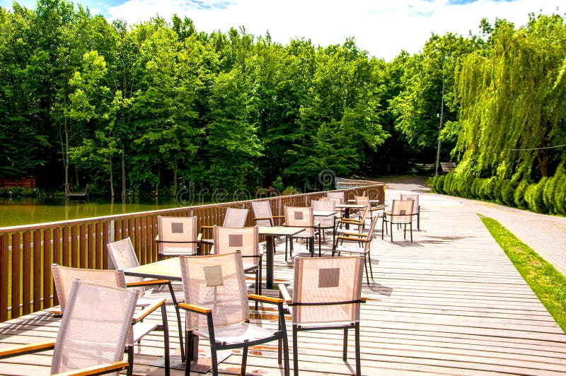 Träbro med ett staket som tabeller och stolar lokaliseras på Sommarkaf? Det ?r sommar utanf?r Solen ?r gl?nsande royaltyfria foton Träbro med ett staket som tabeller och stolar lokaliseras på Sommarkaf? Det ?r sommar utanf?r Solen ?r gl?nsande royaltyfria foton