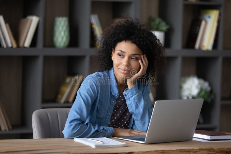 Träumliche glückliche tausendjährige afrikanische Amerikanerin arbeitet an Computer. lizenzfreie stockfotos
