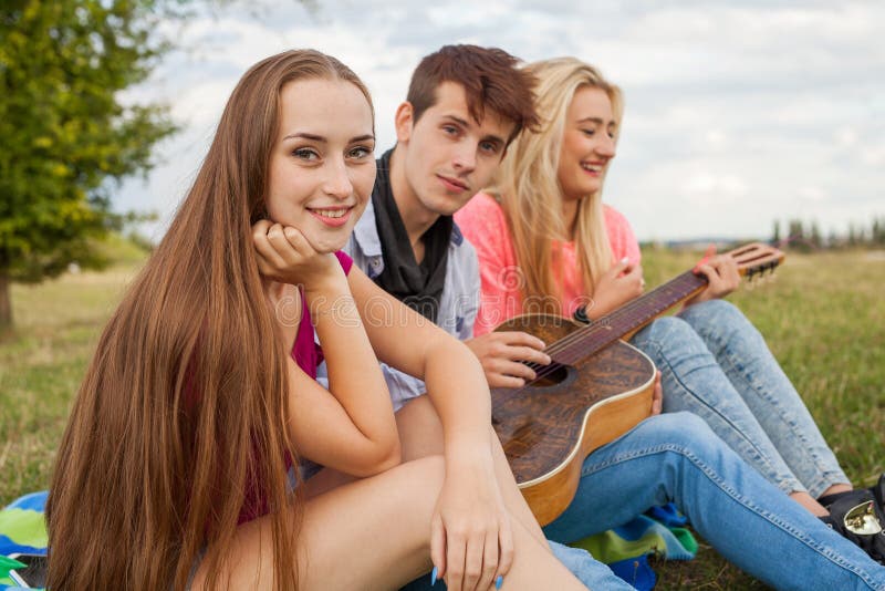 Três amigos com a guitarra que senta-se na cobertura no parque foto de stock royalty free Três amigos com a guitarra que senta-se na cobertura no parque foto de stock royalty free