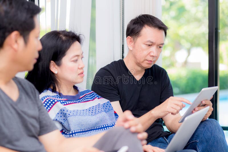 Três amigos na linha com dispositivos múltiplos e no assento de fala em um sofá na sala de visitas em uma casa fotografia de stock royalty free Três amigos na linha com dispositivos múltiplos e no assento de fala em um sofá na sala de visitas em uma casa fotografia de stock royalty free