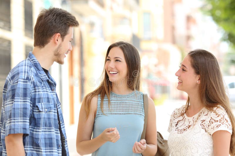 Three happy friends talking taking a conversation on the street in a sunny day with buildings in the background. Three happy friends talking taking a conversation on the street in a sunny day with buildings in the background