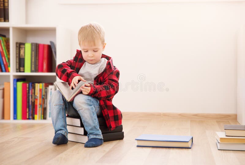 Três anos de criança idosa que senta-se entre livros em casa imagens de stock Três anos de criança idosa que senta-se entre livros em casa imagens de stock