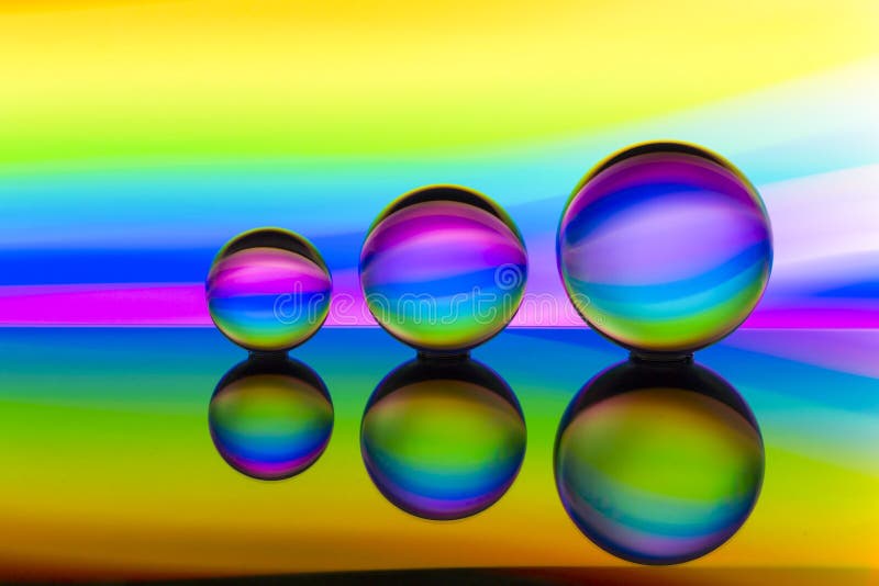 Três bolas de cristal de vidro em seguido com um arco-íris da pintura clara colorida atrás deles fotos de stock Três bolas de cristal de vidro em seguido com um arco-íris da pintura clara colorida atrás deles fotos de stock