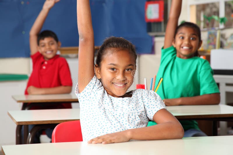 Three happy young primary school children signalling they know the answer with hands raised in class - Canon 5D MKII. Three happy young primary school children signalling they know the answer with hands raised in class - Canon 5D MKII