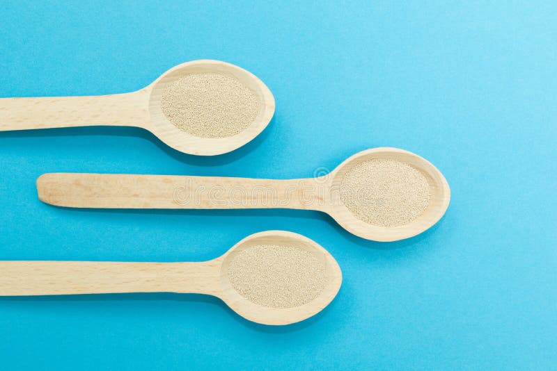 Três colheres de madeira com o fermento seco imediato isolado em um fundo azul O fermento é o ingrediente principal da massa fres fotografia de stock Três colheres de madeira com o fermento seco imediato isolado em um fundo azul O fermento é o ingrediente principal da massa fres fotografia de stock