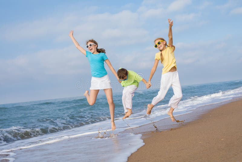 Três crianças felizes que correm na praia no tempo do dia fotografia de stock Três crianças felizes que correm na praia no tempo do dia fotografia de stock
