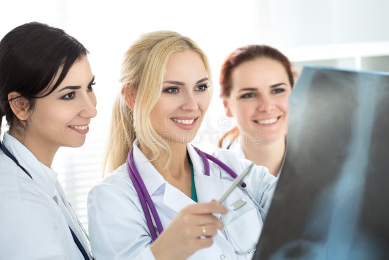 Três doutores fêmeas de sorriso que olham a imagem do raio X foto de stock Três doutores fêmeas de sorriso que olham a imagem do raio X foto de stock