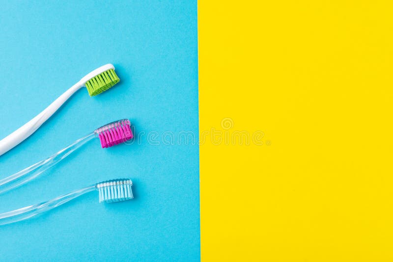 Tr?s escovas de dentes pl?sticas em um azul colorido e em um fundo amarelo, fim acima foto de stock Tr?s escovas de dentes pl?sticas em um azul colorido e em um fundo amarelo, fim acima foto de stock