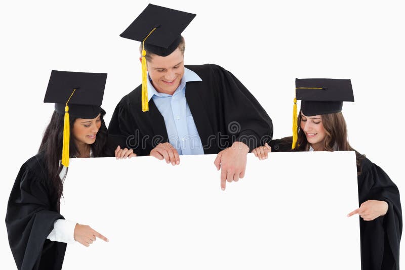 Três graduados que apontam ao sinal vazio foto de stock royalty free Três graduados que apontam ao sinal vazio foto de stock royalty free