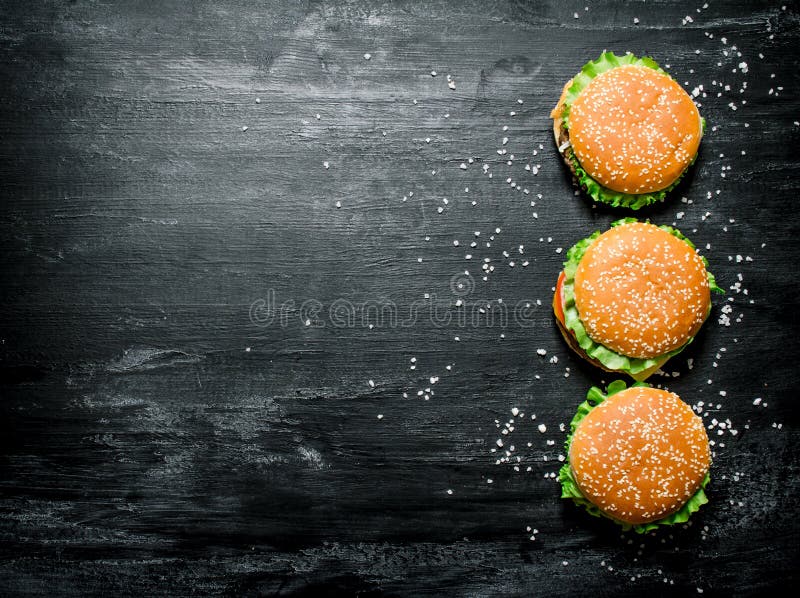 Três hamburgueres com carne, queijo e os legumes frescos imagem de stock Três hamburgueres com carne, queijo e os legumes frescos imagem de stock