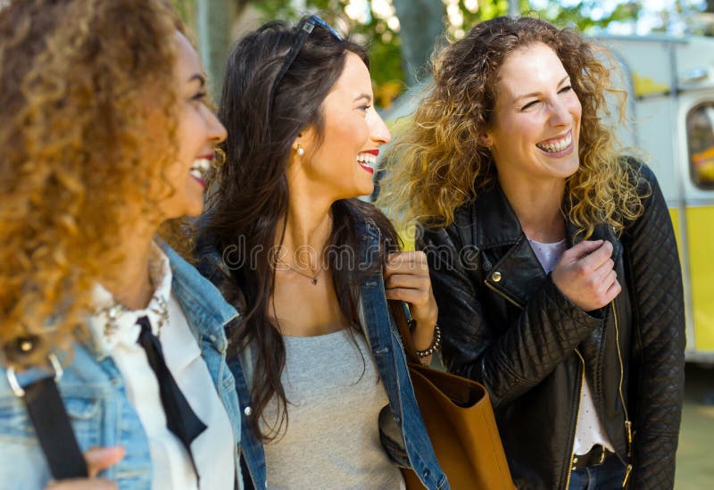 Três jovens mulheres bonitas que andam e que falam na rua fotografia de stock royalty free Três jovens mulheres bonitas que andam e que falam na rua fotografia de stock royalty free
