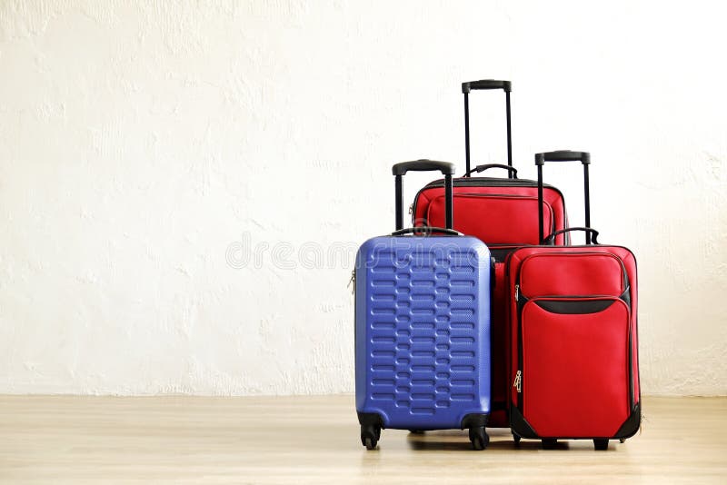 Three suitcases of different size, big & small, red textile and blue hard shell luggage with extended telescopic handle. Family trip concept. Copy space, white wall background. Fully packed baggage. Three suitcases of different size, big & small, red textile and blue hard shell luggage with extended telescopic handle. Family trip concept. Copy space, white wall background. Fully packed baggage.