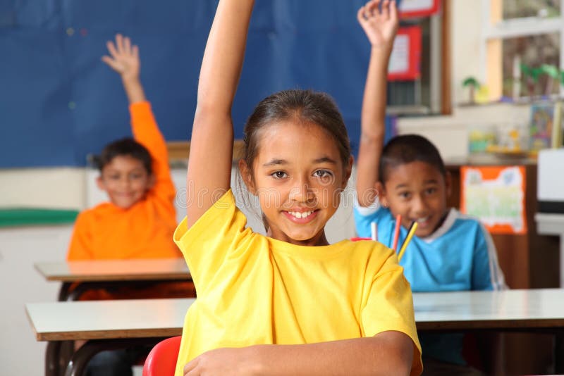 Three cheerful young primary school children indicating they know the answer with hands raised in class - Canon 5D MKII. Three cheerful young primary school children indicating they know the answer with hands raised in class - Canon 5D MKII