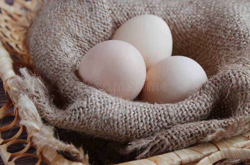 Três ovos frescos encontram-se em um guardanapo bege em uma cesta imagem de stock royalty free Três ovos frescos encontram-se em um guardanapo bege em uma cesta imagem de stock royalty free