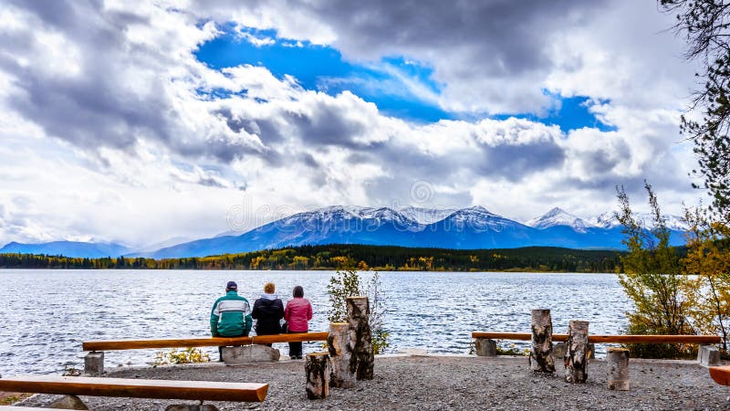 Três pessoas que apreciam a vista do lago pyramid com a montanha dos assobiadores no fundo em Jasper National Park imagens de stock Três pessoas que apreciam a vista do lago pyramid com a montanha dos assobiadores no fundo em Jasper National Park imagens de stock