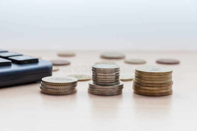 Três pilhas de moedas e uma calculadora estão na tabela foto de stock royalty free Três pilhas de moedas e uma calculadora estão na tabela foto de stock royalty free