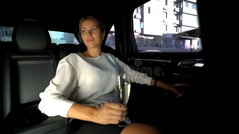Trött kvinna som dricker champagne på bilbackseaten som hem kör med den privata chauffören royaltyfri bild Trött kvinna som dricker champagne på bilbackseaten som hem kör med den privata chauffören royaltyfri bild