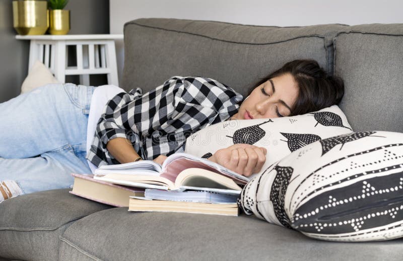 Trött kvinna som sover med boken i händerna på soffan i vardagsrummet arkivfoto