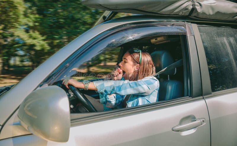 Trött ung kvinna som kör bilen och att gäspa royaltyfri fotografi Trött ung kvinna som kör bilen och att gäspa royaltyfri fotografi