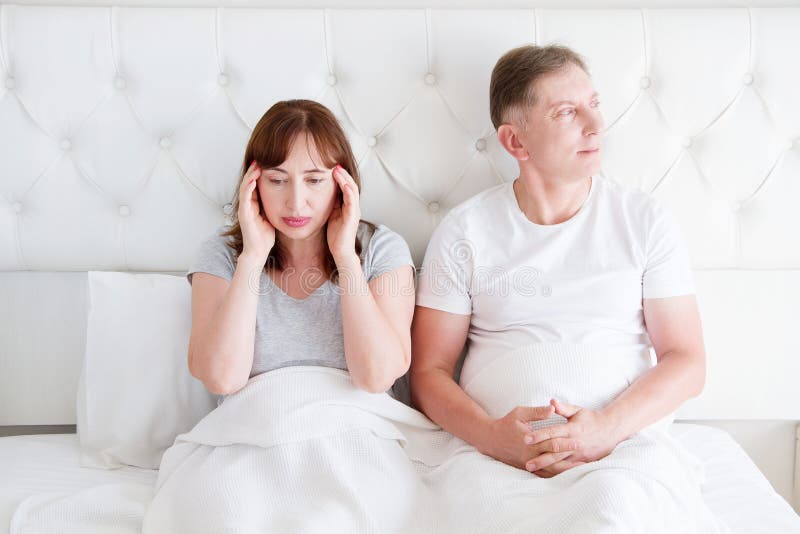 Trötta mellersta ålderfamiljpar i säng Kvinnakänseln smärtar och migrän i huvud Starkt spänningshuvudvärk och spänningsbegrepp royaltyfri bild Trötta mellersta ålderfamiljpar i säng Kvinnakänseln smärtar och migrän i huvud Starkt spänningshuvudvärk och spänningsbegrepp royaltyfri bild