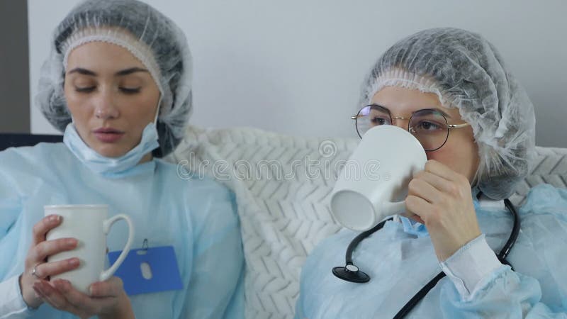 Trötta, sorgliga kvinnliga läkare som dricker kaffe på soffan. frustrerade läkare som vilar när de tar en paus och dricker en drin stock video