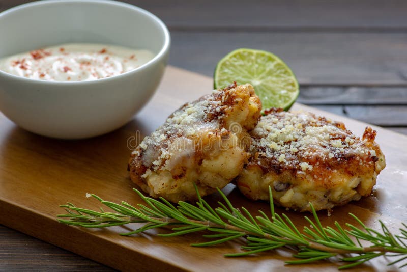 TTwo shrimp cakes on a cutting board with a lemon garlic dipping sauces lemon wedge and a stem or rosemary on a wooden table.. royalty free stock photography TTwo shrimp cakes on a cutting board with a lemon garlic dipping sauces lemon wedge and a stem or rosemary on a wooden table.. royalty free stock photography
