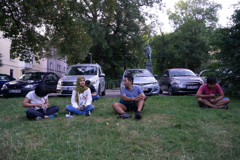 TUBINGEN/GERMANY- 31 LUGLIO 2018: Una serie di turisti asiatici stavano sedendo sul prato inglese, vicino al parcheggio, parlante immagini stock libere da diritti TUBINGEN/GERMANY- 31 LUGLIO 2018: Una serie di turisti asiatici stavano sedendo sul prato inglese, vicino al parcheggio, parlante immagini stock libere da diritti