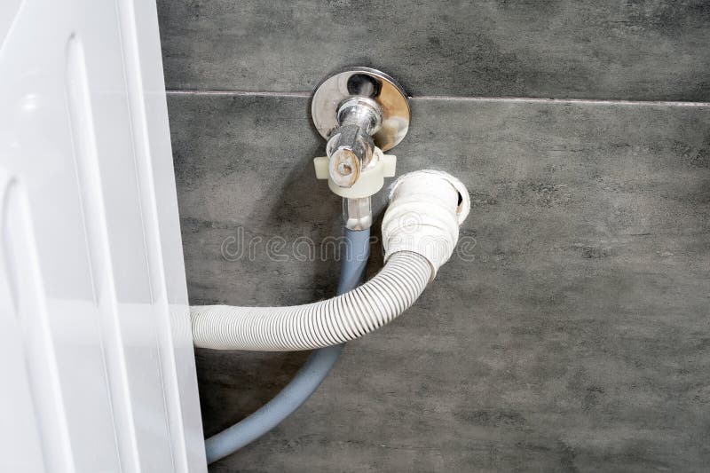 Dirty drain and water hoses for the washing machine running into a wall covered with gray concrete tile. Design options in a comfortable modern bathroom. Dirty drain and water hoses for the washing machine running into a wall covered with gray concrete tile. Design options in a comfortable modern bathroom