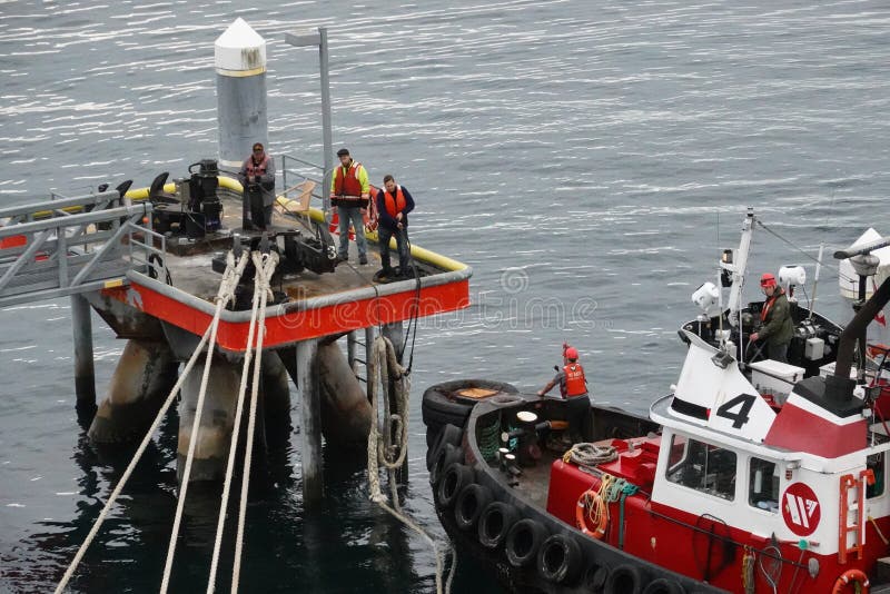 A tug boat drags the boat dock lines from a cruise ship to the dock to be tied up