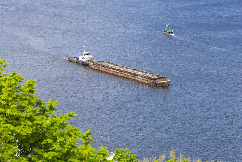 A tug boat hauls a large, empty barge down wide Dnipro river dirung sunny day. Seafaring, navigation on river royalty free stock photography A tug boat hauls a large, empty barge down wide Dnipro river dirung sunny day. Seafaring, navigation on river royalty free stock photography