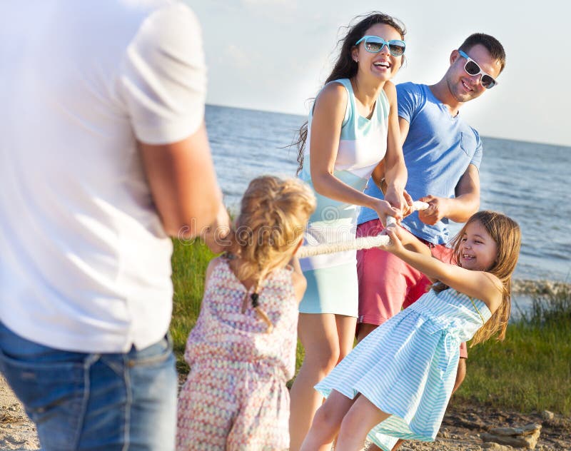 Tug of war - family playing on the beach. Summer holiday and family power concept