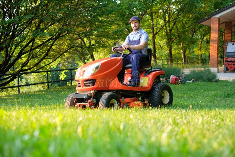 Tuinman die een berijdende grasmaaimachine in tuin drijven stock afbeelding Tuinman die een berijdende grasmaaimachine in tuin drijven stock afbeelding