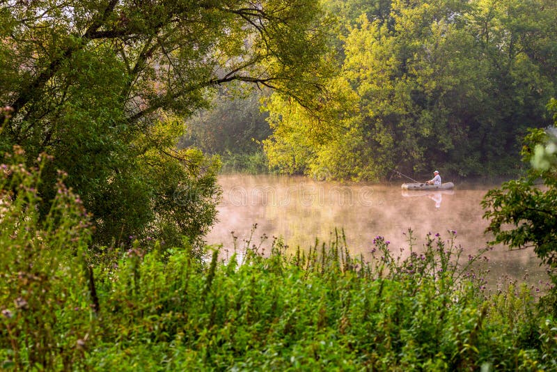 TULA, RUSSIA - AUGUST 12, 2013: A man fishing on river at inflatable boat at foggy summer morning under green foliage royalty free stock image TULA, RUSSIA - AUGUST 12, 2013: A man fishing on river at inflatable boat at foggy summer morning under green foliage royalty free stock image