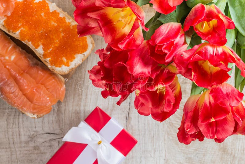 Tulipanes, regalo y bocadillos rojos con el caviar y los salmones rojos en fondo de madera foto de archivo Tulipanes, regalo y bocadillos rojos con el caviar y los salmones rojos en fondo de madera foto de archivo
