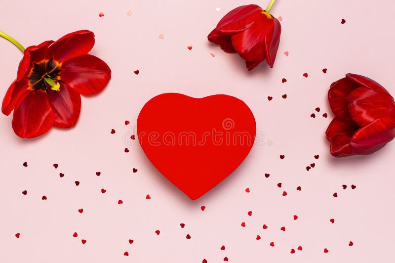 Tulipas vermelhas, coração vermelho caixa de presente dada forma, confete no espaço colocado liso cor-de-rosa pastel da cópia da fotografia de stock Tulipas vermelhas, coração vermelho caixa de presente dada forma, confete no espaço colocado liso cor-de-rosa pastel da cópia da fotografia de stock