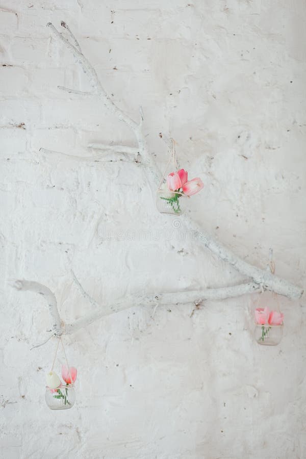 Tulips in Vases Hang on a Decorative Branch on a Wall with White Bricks