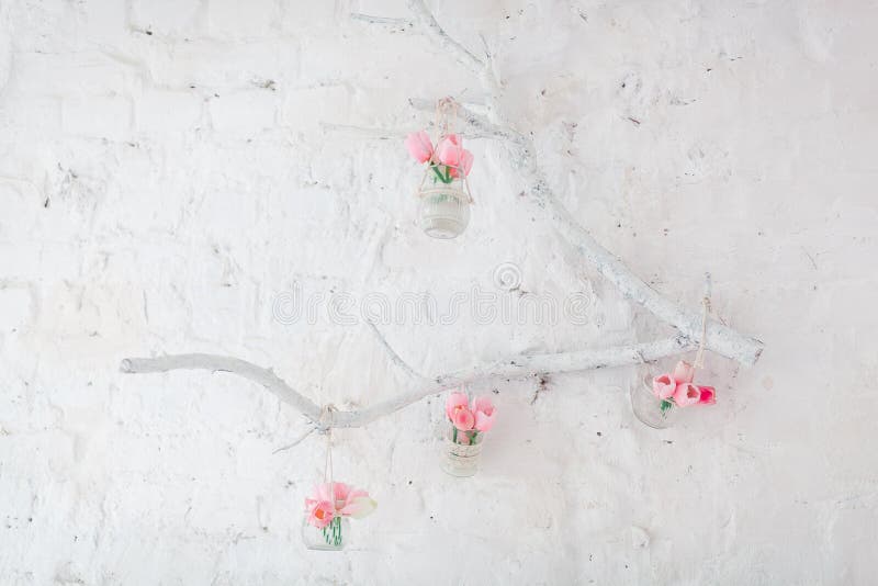 Tulips in Vases Hang on a Decorative Branch on a Wall with White Bricks