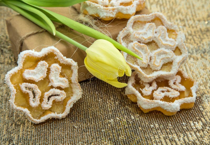 Tulipán en un fondo de paquetes de oro con un regalo embalado y galletas delicadas foto de archivo Tulipán en un fondo de paquetes de oro con un regalo embalado y galletas delicadas foto de archivo