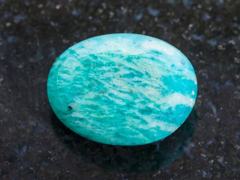 macro shooting of natural mineral rock specimen - tumbled amazonite gemstone (amazon stone) on dark granite background