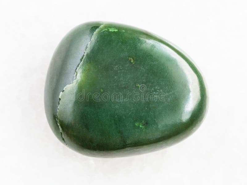 macro shooting of natural mineral rock specimen - tumbled green nephrite gemstone on white marble background