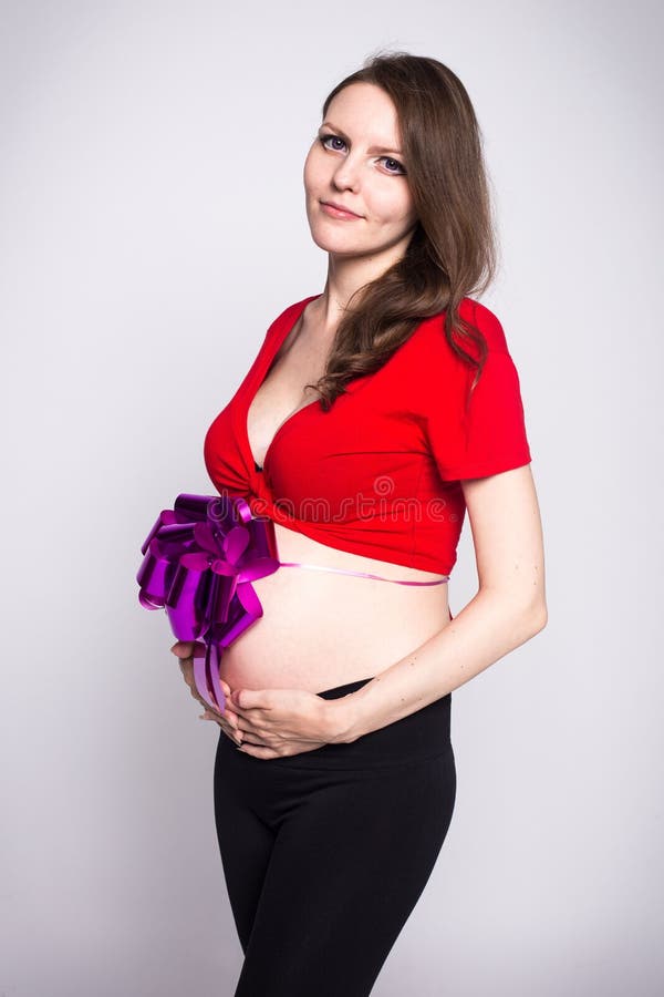 Tunn gravid flicka i en röd blus med den lilla magen som förbindas med en pilbåge arkivbilder Tunn gravid flicka i en röd blus med den lilla magen som förbindas med en pilbåge arkivbilder