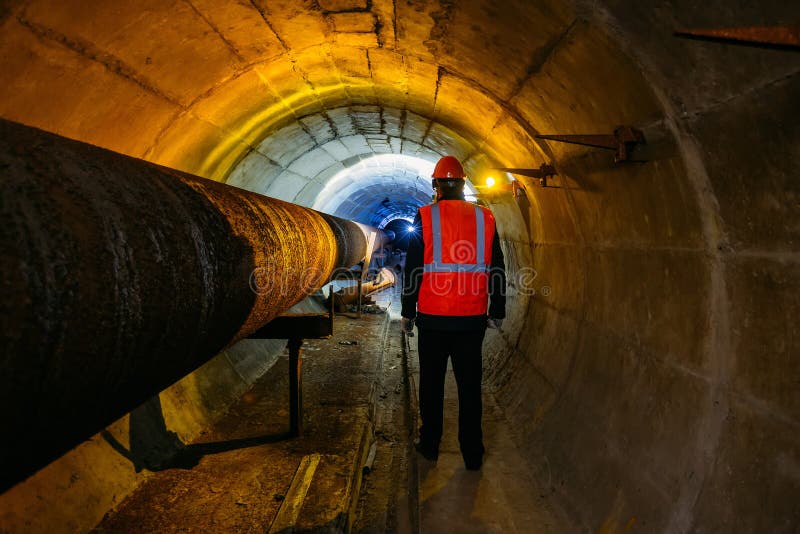 Tunnel worker examines pipeline in underground tunnel royalty free stock photos