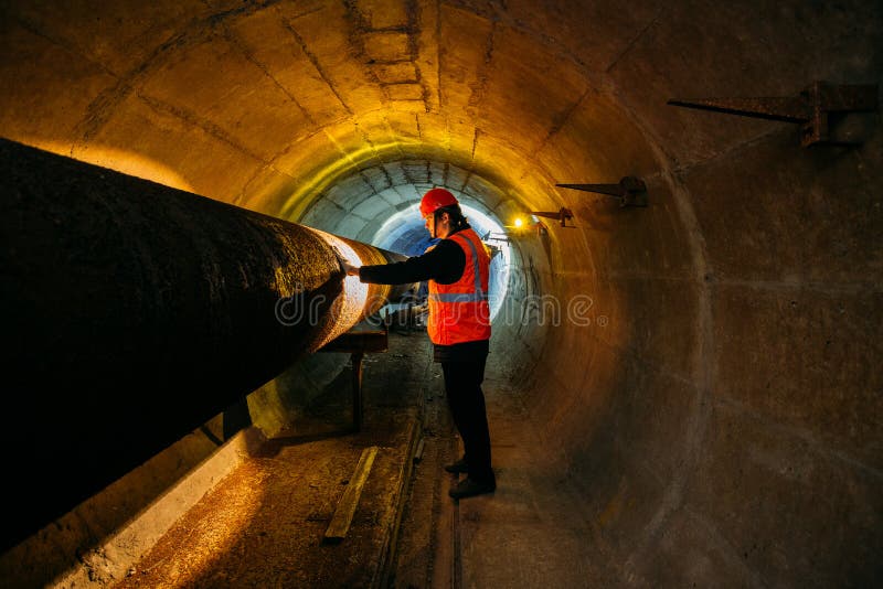 Tunnel worker examines pipeline in underground tunnel stock images