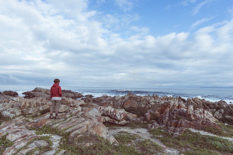 Turista che guarda con binoculare sulla linea rocciosa della costa De Kelders, Sudafrica, famoso per la sorveglianza della balena fotografia stock Turista che guarda con binoculare sulla linea rocciosa della costa De Kelders, Sudafrica, famoso per la sorveglianza della balena fotografia stock