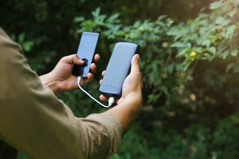 Turista com smartphone e carregador de bateria caminha na floresta de verão. cara com powerbank está perdido na natureza. moderno