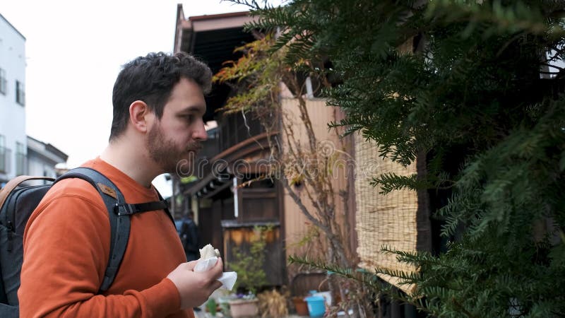 Turista europeo comiendo un nikuman parado en una calle japonesa en takayama.