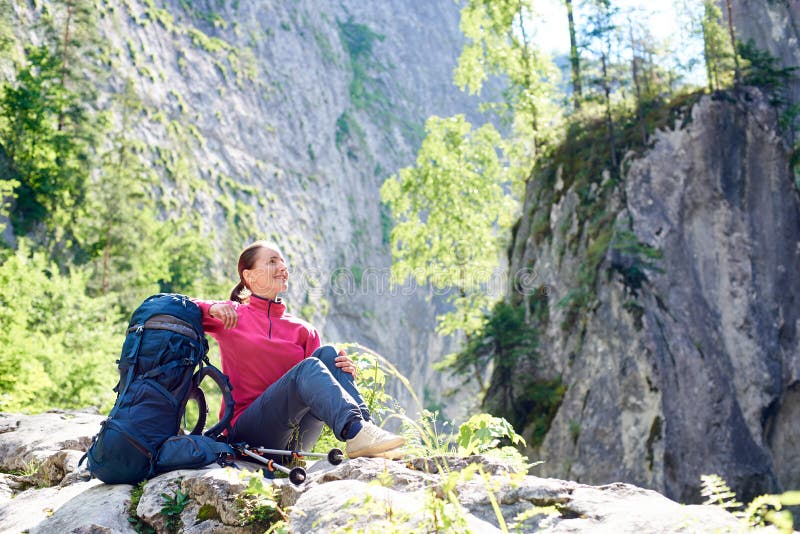 Turista femminile sorridente che riposa sulla bellezza piena d'ammirazione della roccia delle montagne rocciose strabilianti nel fotografie stock libere da diritti Turista femminile sorridente che riposa sulla bellezza piena d'ammirazione della roccia delle montagne rocciose strabilianti nel fotografie stock libere da diritti