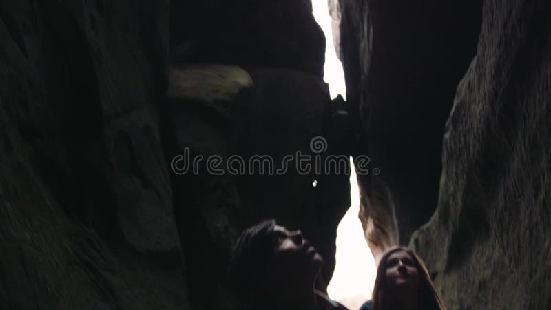 Turistas jovenes que estudian la cueva oscura, llevando a cabo sus manos, y moviéndose hacia la cámara